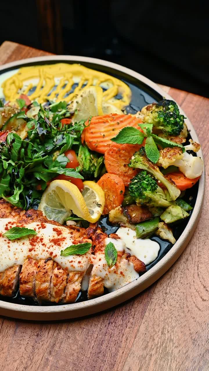 Kellner serviert einen Teller mit gegrilltem Lachs und geröstetem Gemüse. Hand hält einen Teller mit gegrilltem Lachs, weißer Soße, gerösteten Karotten, Brokkoli und frischem Salat in einem Restaurant.