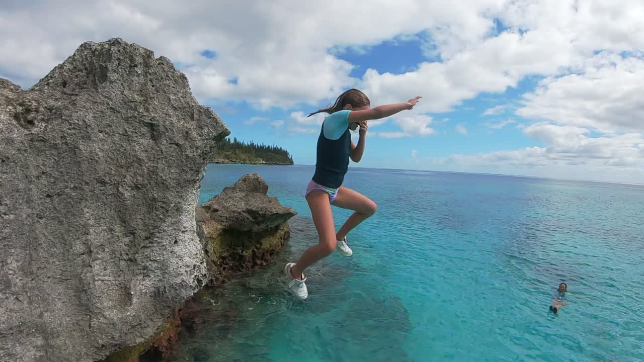 Young girl cliff jumping in tropical sea, action camera follow shot, slow motion