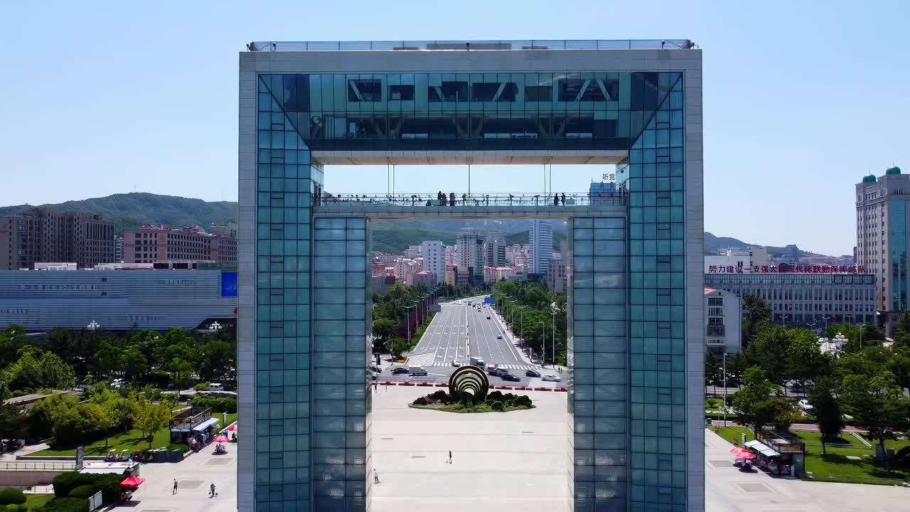 Cinematic aerial drone pullback showing Xingfu park arch gate portal with cityscape background
