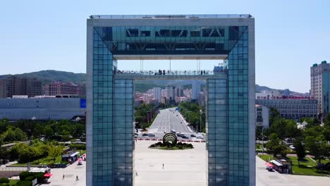 cinematic aerial drone pullback showing xingfu park arch gate portal with cityscape background