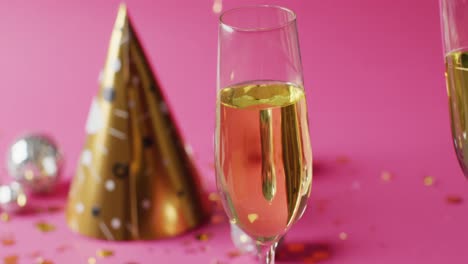 Video-of-two-full-champagne-glasses-with-gold-party-hat-and-bauble-on-pink-background