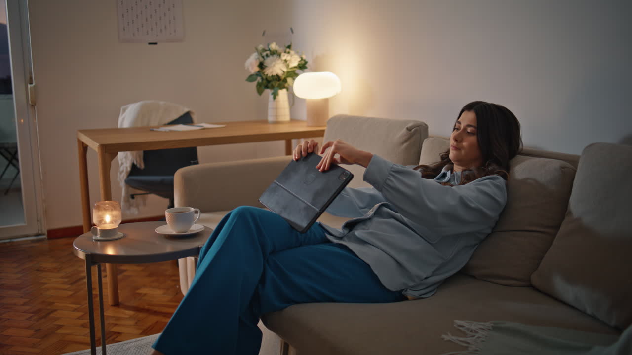 calma chica abriendo la almohadilla mirando la pantalla en el sofá de la casa de la noche. mujer sofá relajante