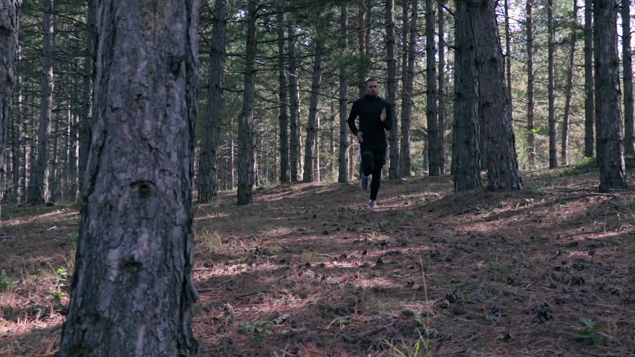 Athlete running through a forest with big trees slow motion