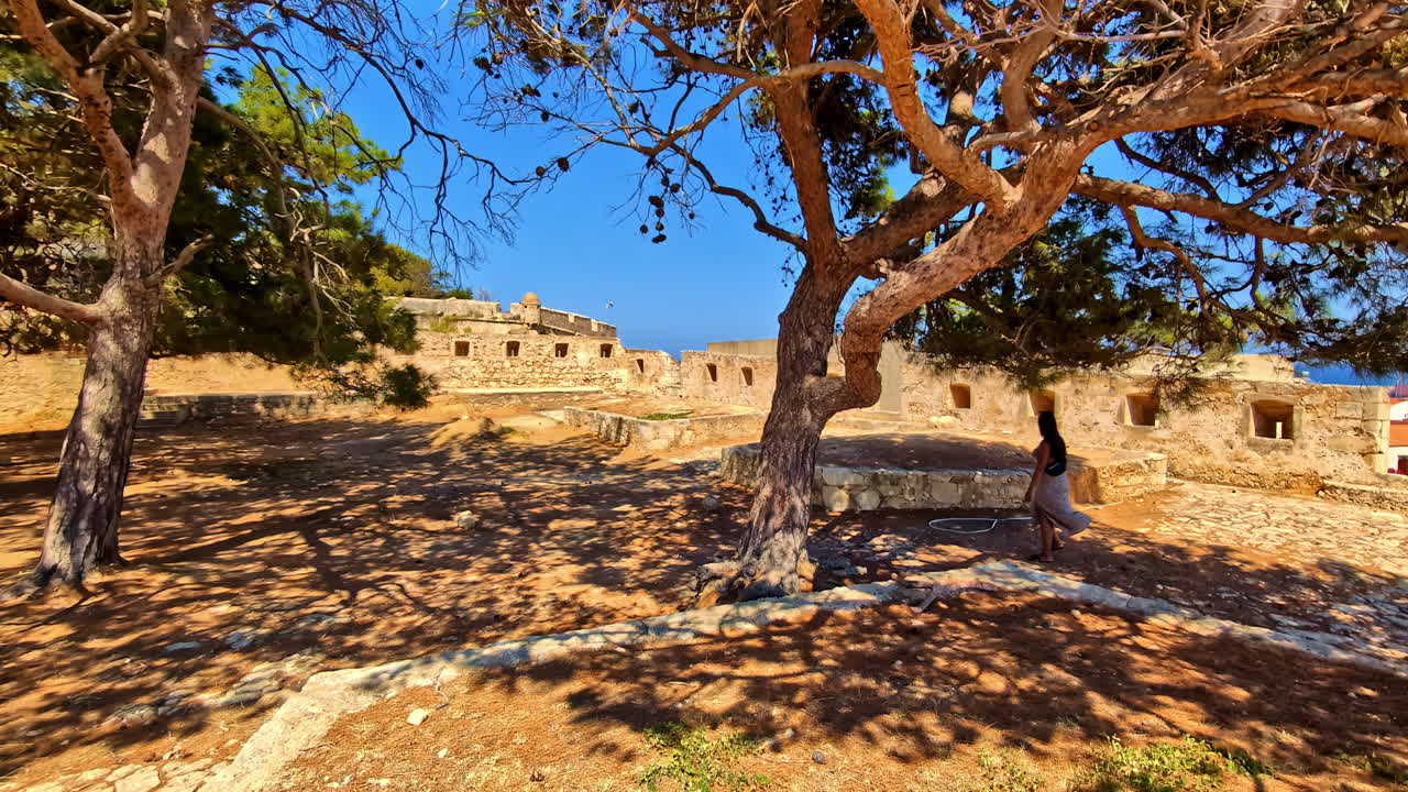 Young, attractive, female tourist filming at medieval fortress ruins at Rethymno, Crete, Greece