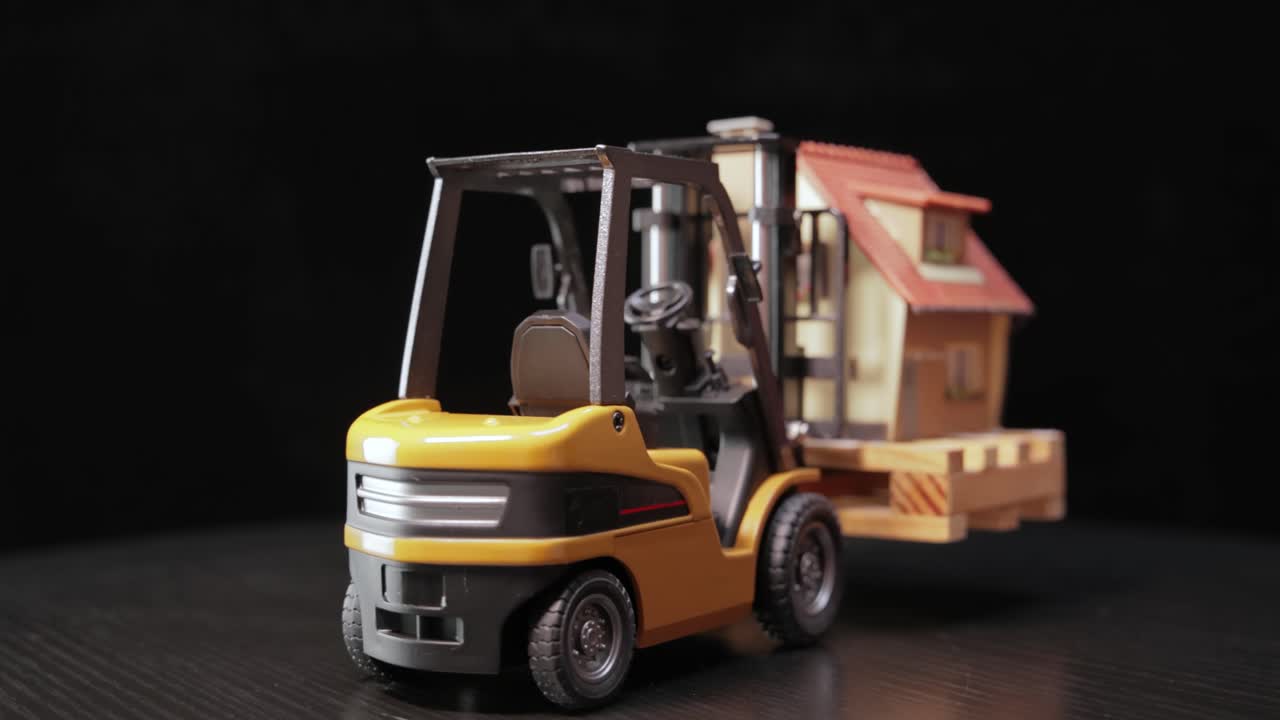 포크리프트 트럭은 팔레트 위에 집을 들고 있습니다. 화물 운송과 물류의 개념, 집과 건물의 건설.