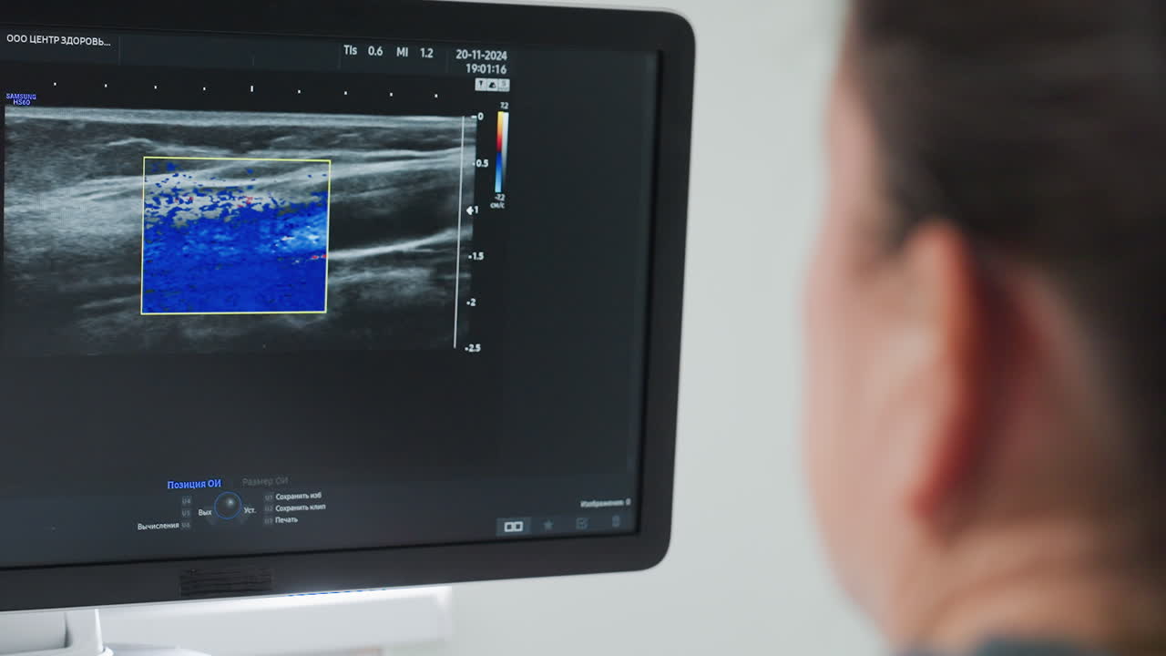Radiology technician carefully observes diagnostic imaging screen displaying real-time internal scan activity during medical examination, analyzing patient data with focus and precision