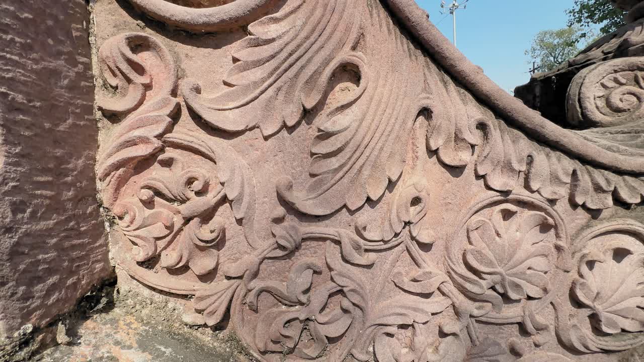 Camera tracks across an ornate stone carving filled with swirling floral motifs, rounded leaf patterns, and finely sculpted curves, highlighting the craftsmanship in warm sunlight
