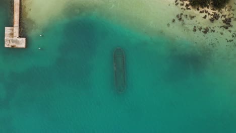 Birds-eye-view-of-rusty-shipwreck-sitting-on-seafloor-in-turquoise-ocean