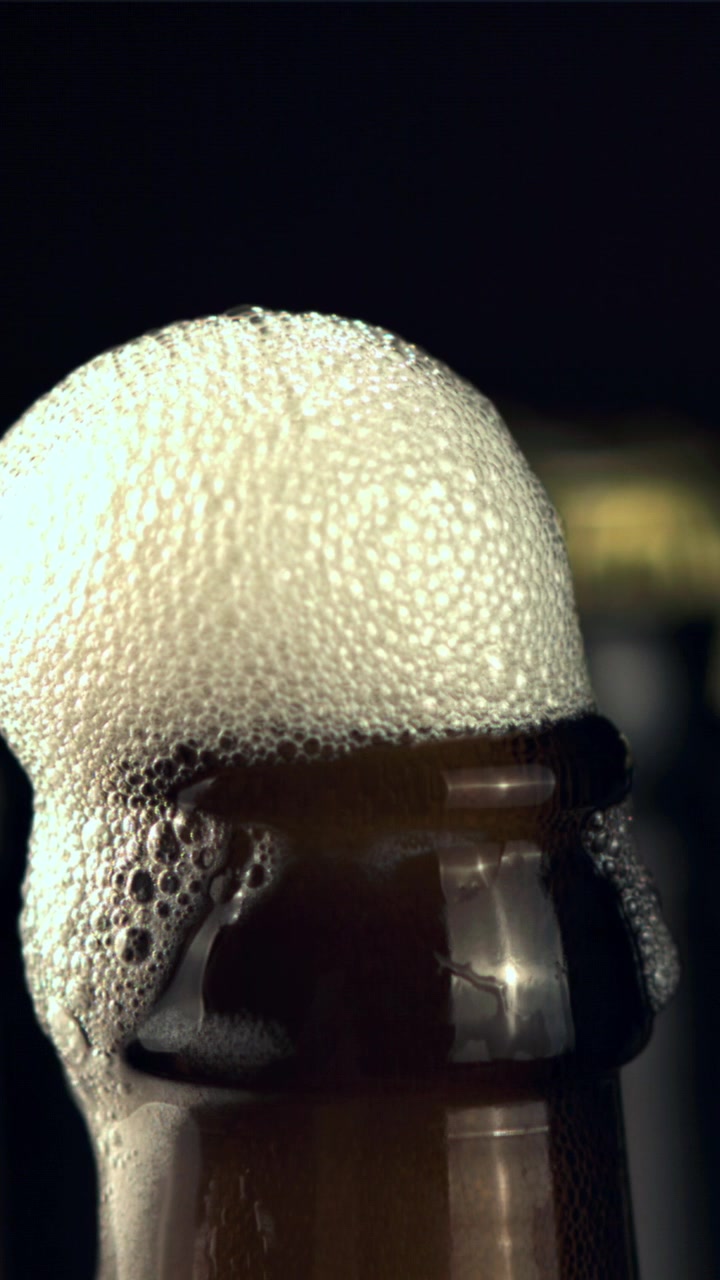 Schiuma di birra rinfrescante che trabocca da una bottiglia marrone