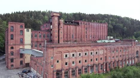 Lost-Place-Fabrik-In-Ostdeutschland-Aus-Sozialistischen-Zeiten-Drohne-Fährt-Rückwärts-Hinaus,-Während-Sie-An-Einem-Bewölkten-Tag-Das-Gebäude-Im-Blick-Behält