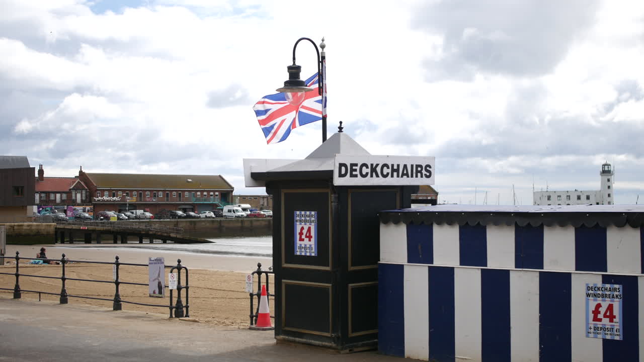 A deckchair hire kiosk with a Union Jack flag stands near the sand and lighthouse along the seafront in Scarborough, North Yorkshire in England