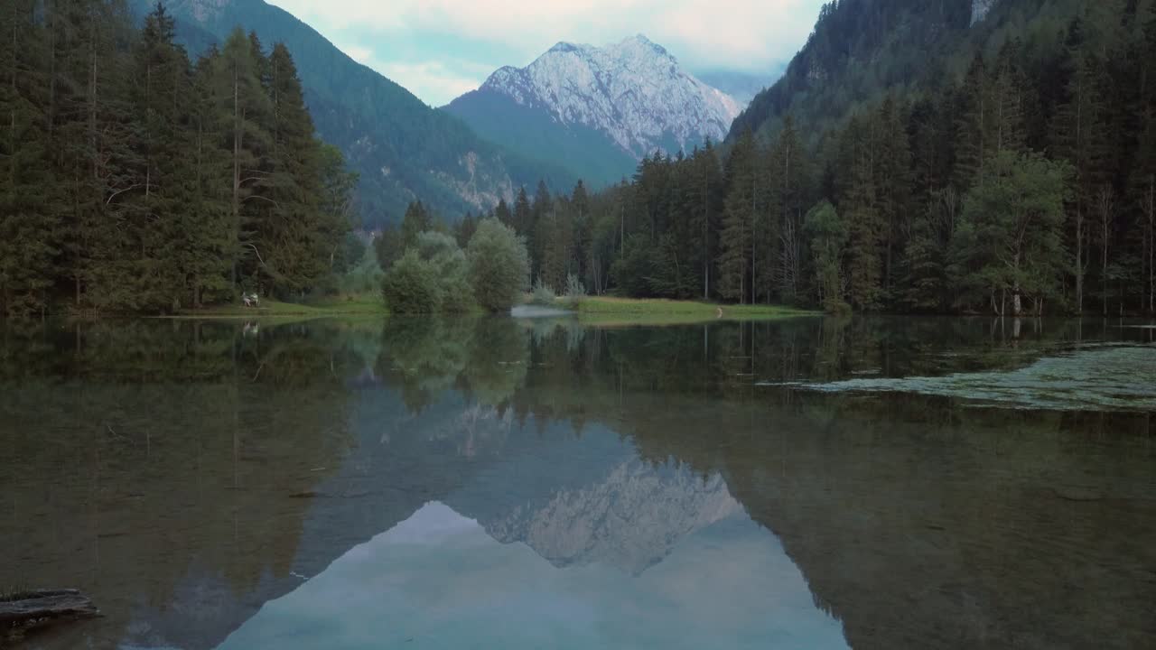 Alpine mountain range reflecting in lake Plansar or Plansarsko jezero in Jezersko, Slovenia in autumn, revealing tilt up shot