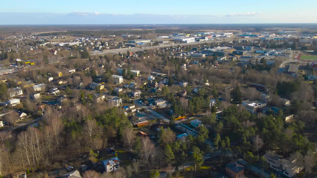 Aerial drone footage of sunny Laagri Saue district with small private houses and apartment buildings visible on the ground during a sunny spring or autumn day. Leafless trees and pines trees visible.