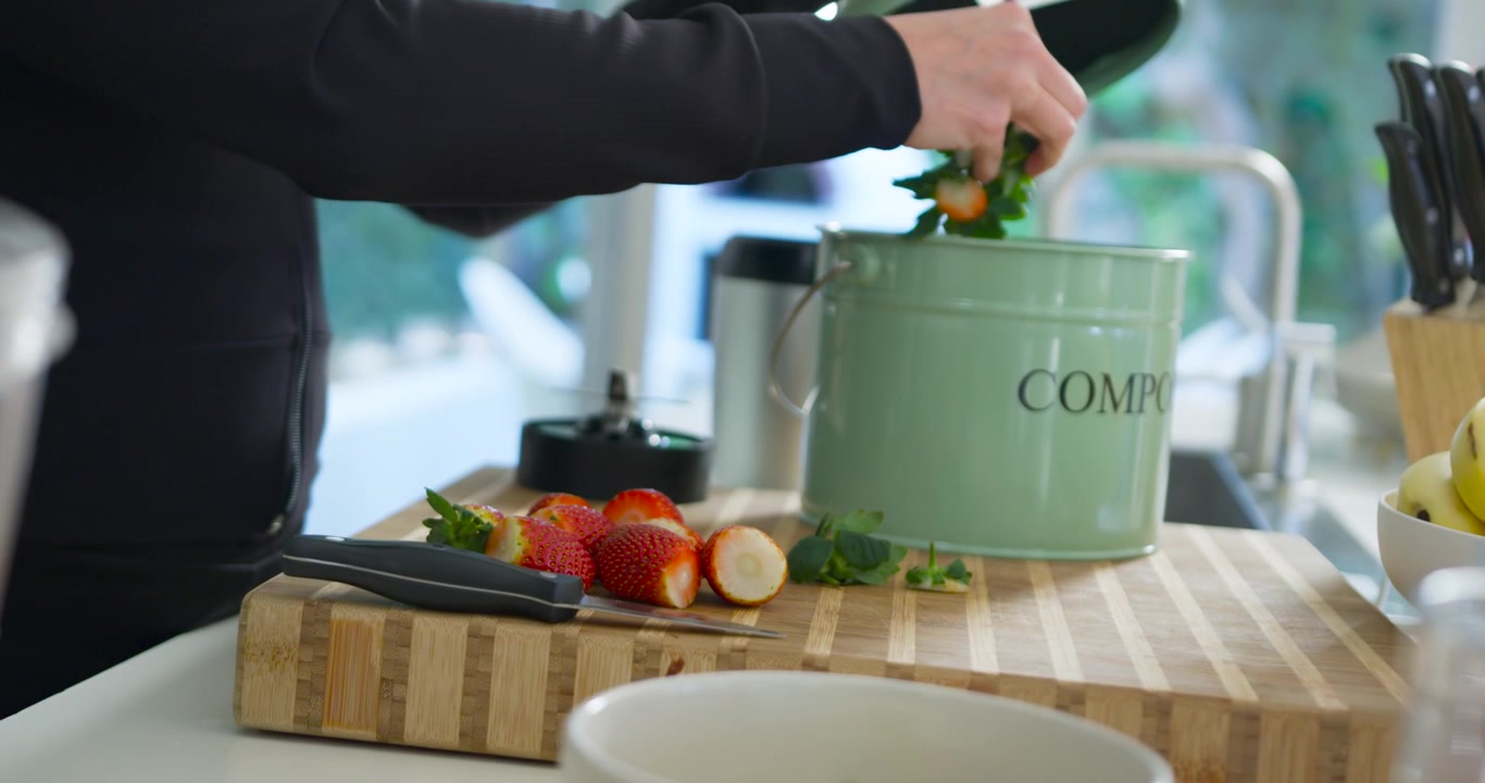 Amies préparant des fruits dans la cuisine, l'une des femmes ramassant les épluchures dans un composteur vert.