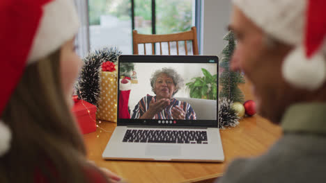 Rückansicht-Eines-Kaukasischen-Paares-Mit-Weihnachtsmützen,-Das-Während-Der-Weihnachtszeit-Einen-Videoanruf-Auf-Dem-Laptop-Führt