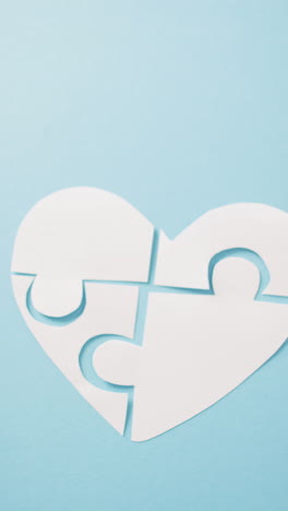 video vertical de forma de corazón blanco en piezas de rompecabezas en fondo azul con espacio de copia