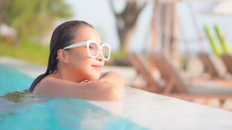 Close-up-of-a-pretty-young-woman-lying-her-head-on-the-edge-of-a-swimming-pool