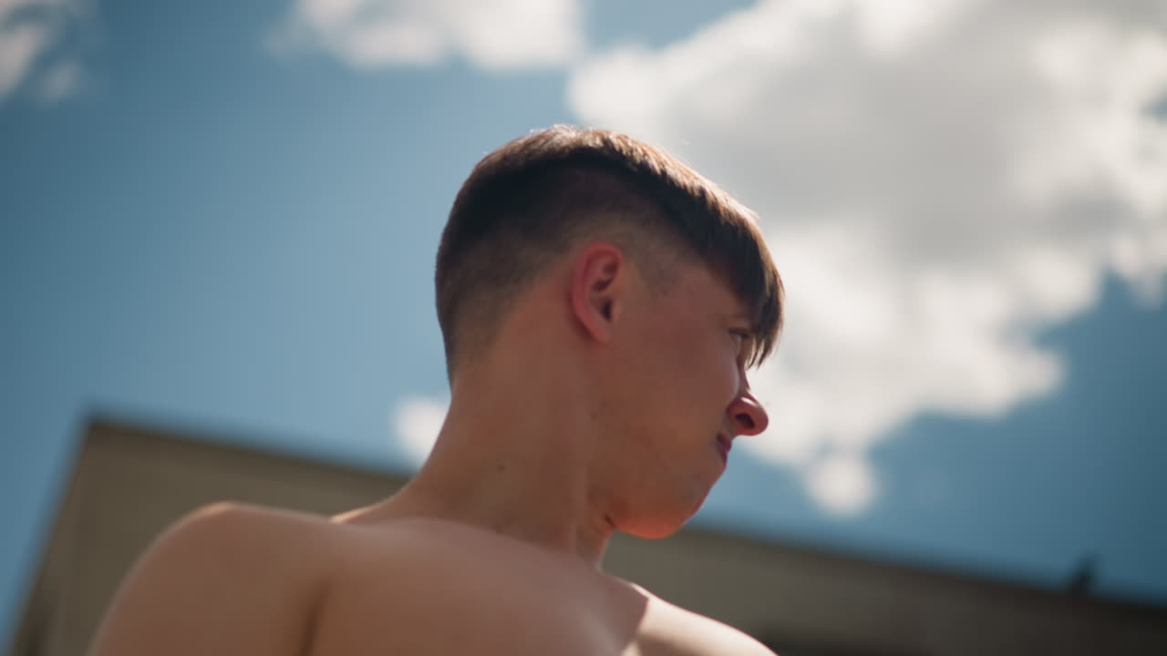 남자가 옷을 들어 올리고, 밝은 하늘을 배경으로 옷을 들어 올리는 사람, 남자가 밝게 빛나는 하늘을 향해 셔츠를 들어 올리고, 개인이 빛나는 하늘 위로 옷감을 높이 들어 올립니다.