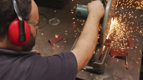 Caucasian-male-factory-worker-at-a-factory-standing-at-a-workbench-and-cutting-a-metal