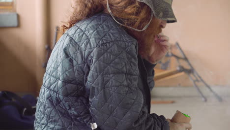 homeless man outdoors near broken bench smoking marijuana joint holding beer can not drinking