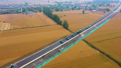 zoom-out aerial of a fleet of driverless, autonomous road rollers and other heavy machinery working on new road construction in rural bozhou, anhui province, china
