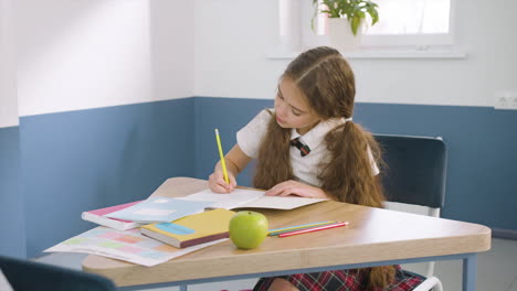 Konzentriertes-Mädchen,-Das-Am-Schreibtisch-Sitzt-Und-Während-Des-Englischunterrichts-In-Der-Schule-In-Ein-Notizbuch-Schreibt