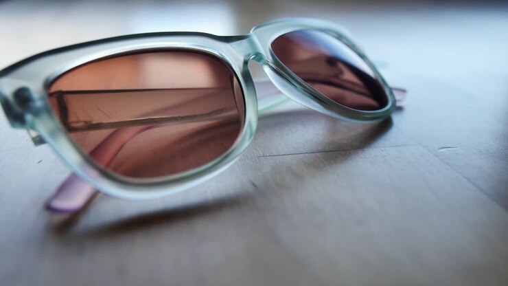 Transparent blue sunglasses being set on light wood table