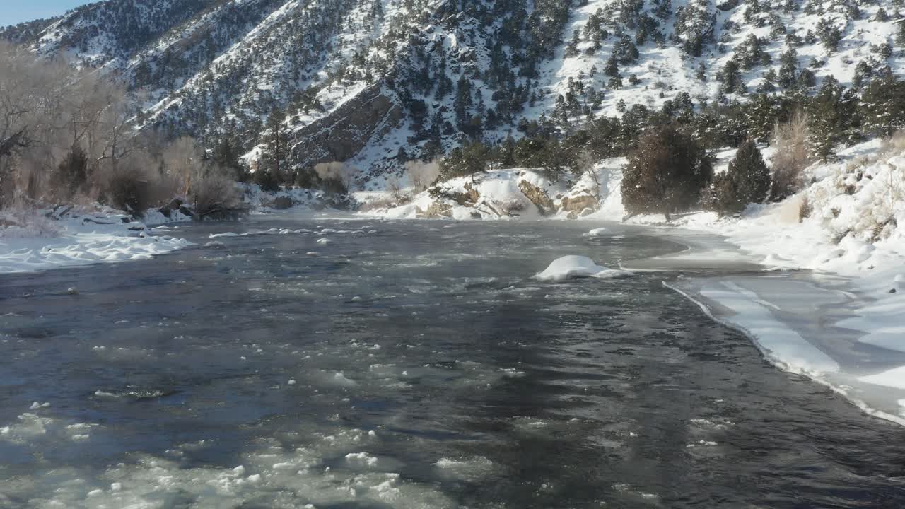 hielo fluyendo por un arroyo de montaña con orillas cubiertas de nieve