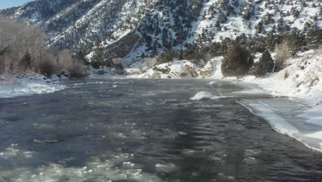 Eis-Fließt-Einen-Gebirgsbach-Hinunter,-Dessen-Ufer-Mit-Schnee-Bedeckt-Sind