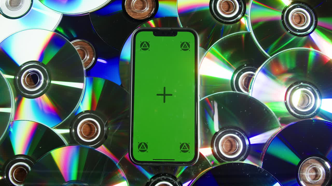 Smartphone with chroma key screen among cd disks close-up. Green screen on mobile phone lays on dvd disk background