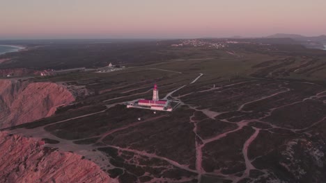 Aerial-view-of-famous-Farol-do-cabo-Espichel-on-edge-of-high-cliff-during-sunset,-Portugal