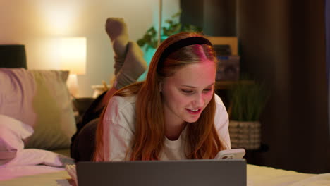 woman on bed using laptop and phone at night