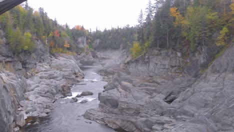 aerial-shot-following-a-beautiful-river-flowing-down-between-the-rocks-surrounded-by-cliffs-and-Autumn-colored-trees