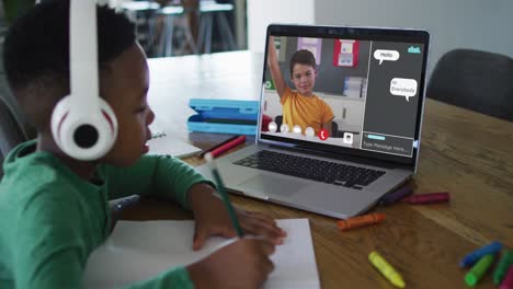 Schoolboy-using-laptop-for-online-lesson-at-home,-with-boy-raisinng-hand-and-web-chat-on-screen