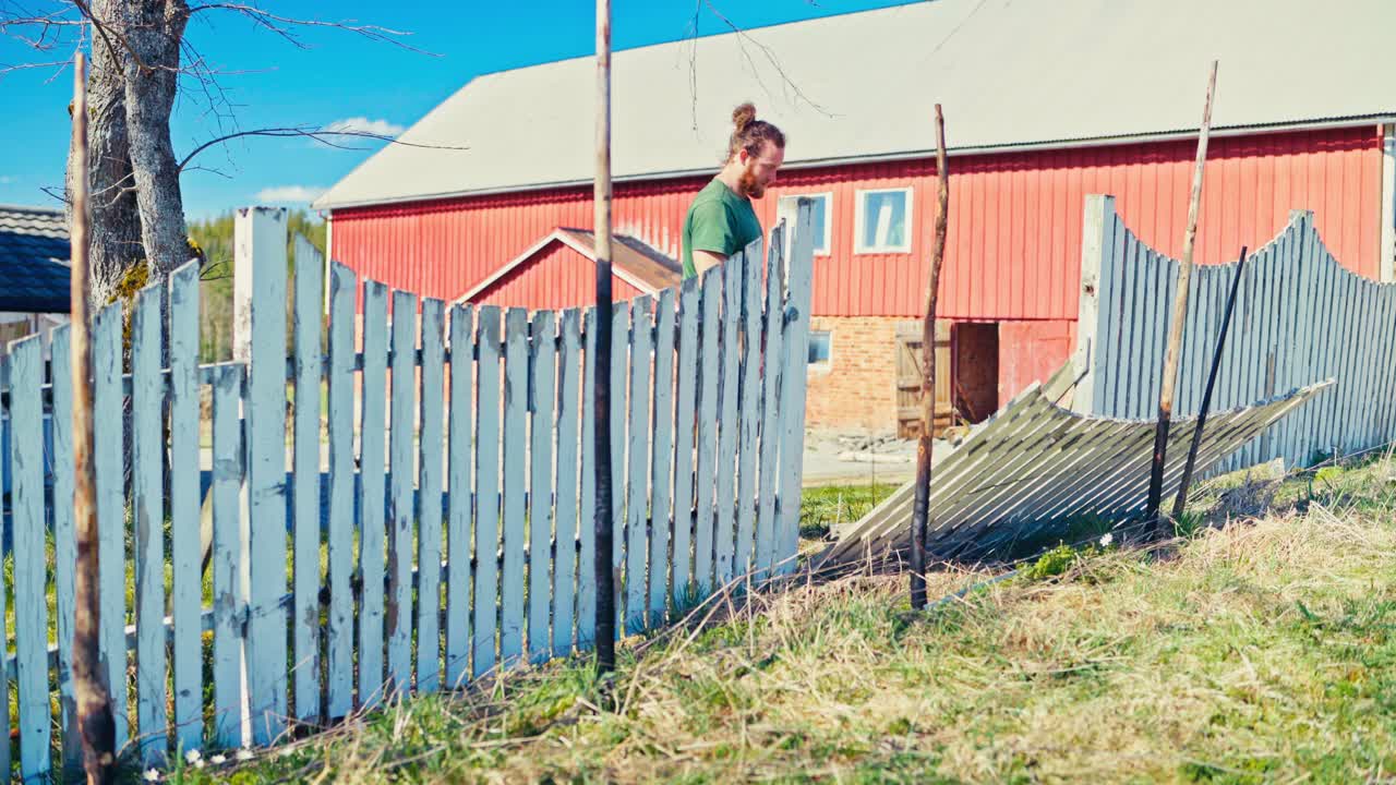 A Man Is Fixing A Wooden Plank Fence On A Sunny Day. Static Shot