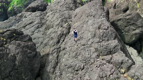 Hiker-precariously-walking-across-a-rugged,-tropical-rocky-boulder-on-the-island-of-Catanduanes,-Philippines
