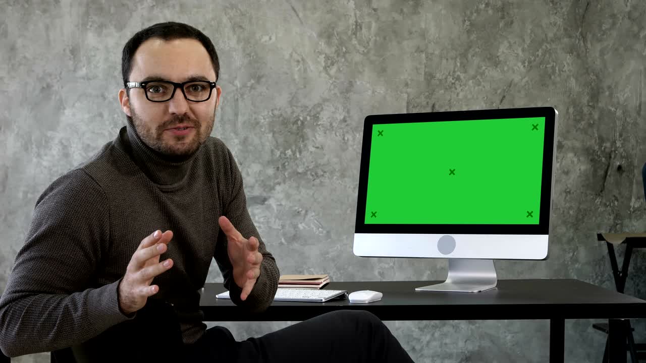 Confident young man looking at camera talking in a very confident way near computer screen. Green Screen Mock-up Display