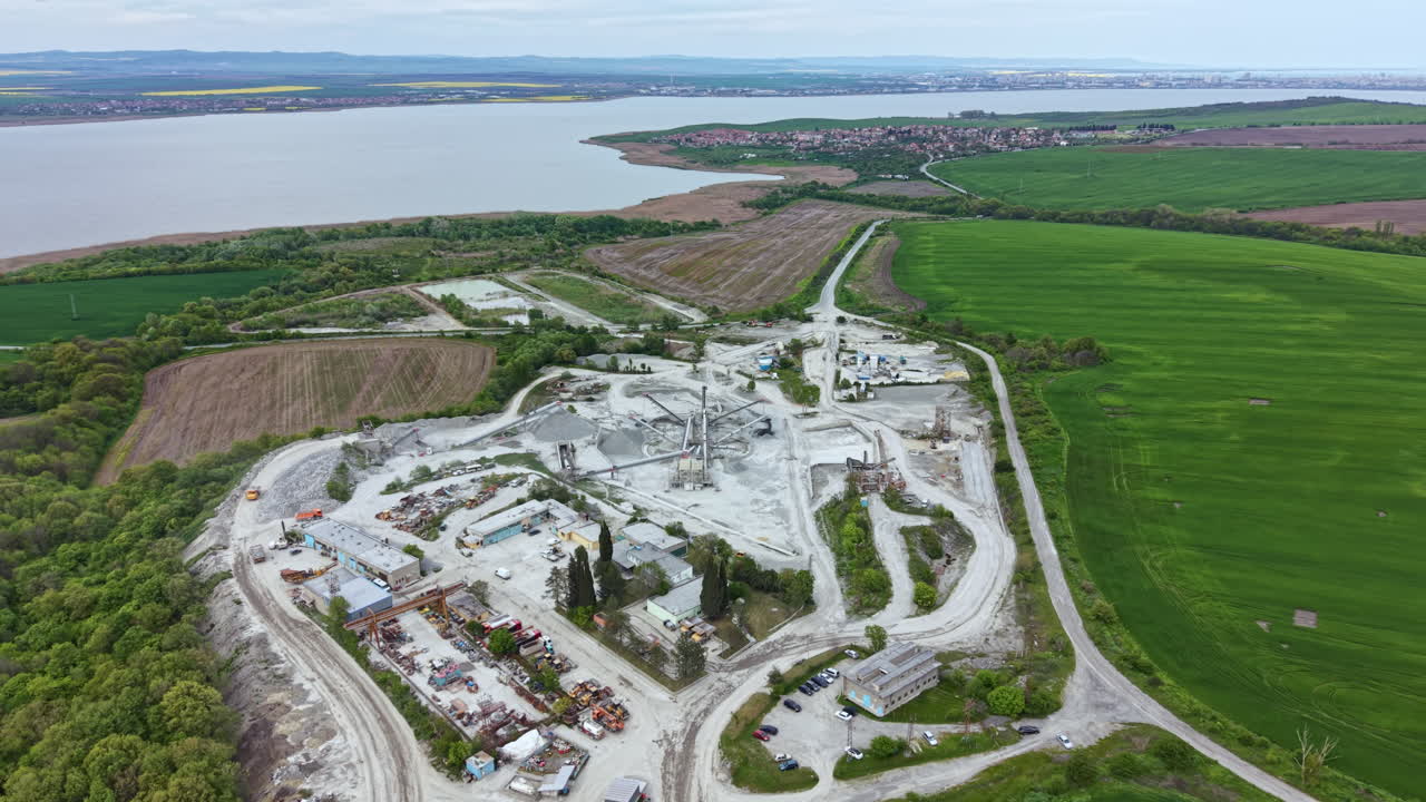 Construction project at a large site near a river with green fields and buildings under development in the background