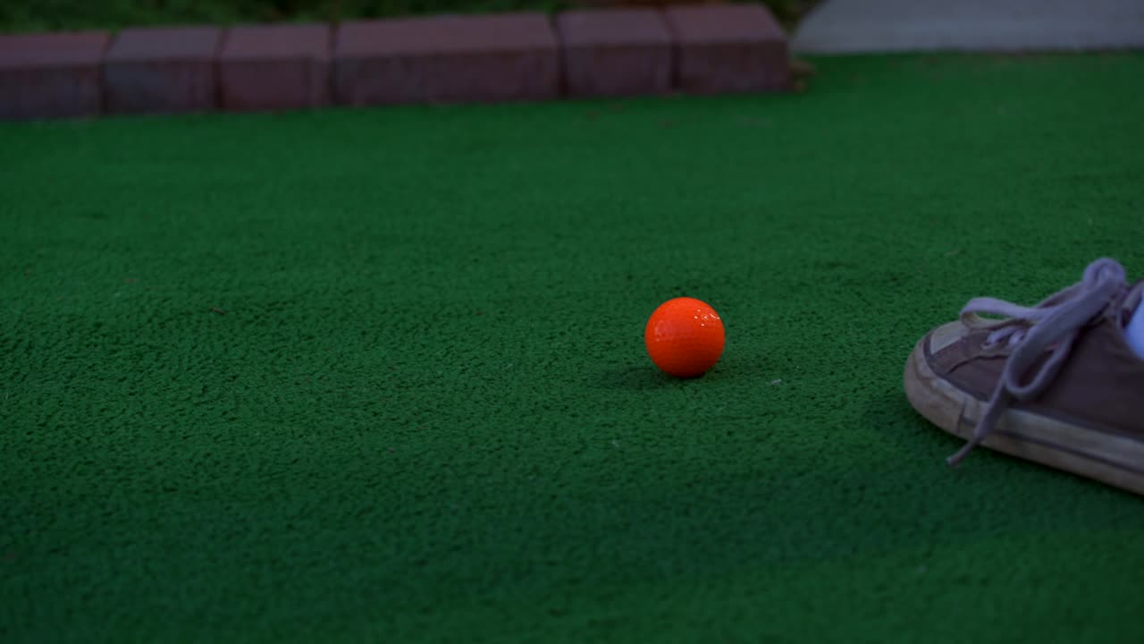 An orange ball getting hit by a putter at a miniature golf course
