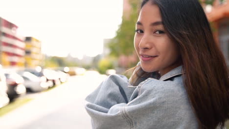 back view of a beautiful young japanese woman walking on the street, turning face and smiling at camera