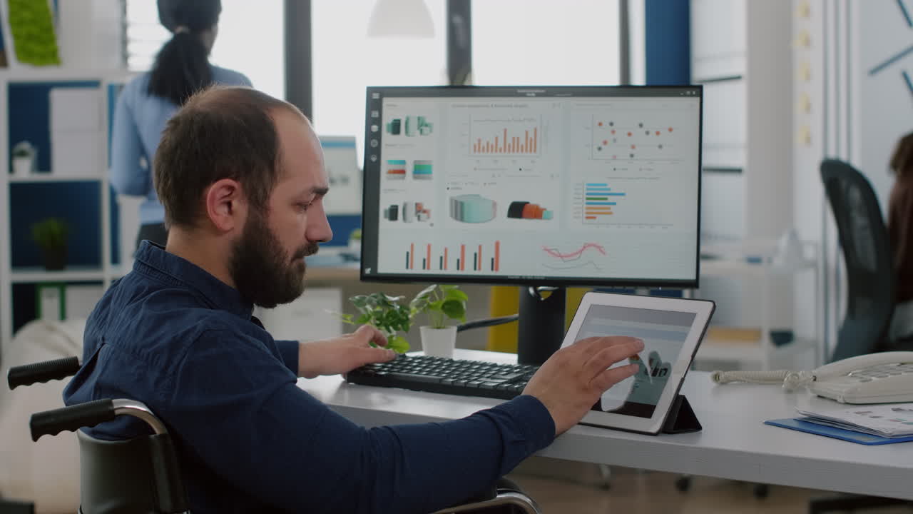 empleado discapacitado sentado en silla de ruedas trabajando en bloc de notas y computadora