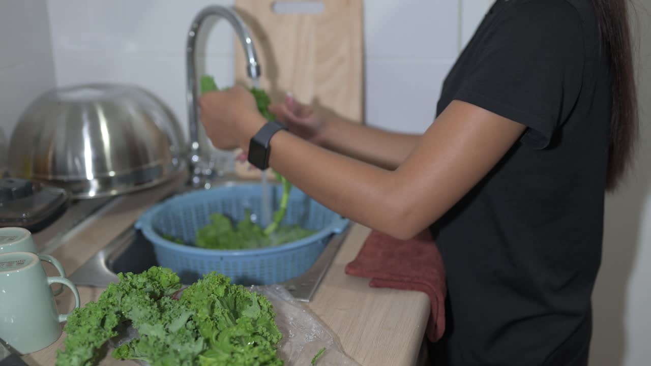Woman preparing and washing fresh kale leaves in home kitchen at night horizontal shot
