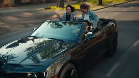 the happy trio ride in a gray convertible with a breeze. the wind develops hair, a happy trip of young friends in denim jackets