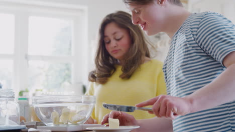 una pareja joven con síndrome de down añadiendo mantequilla a la receta del pastel que están horneando en la cocina en casa
