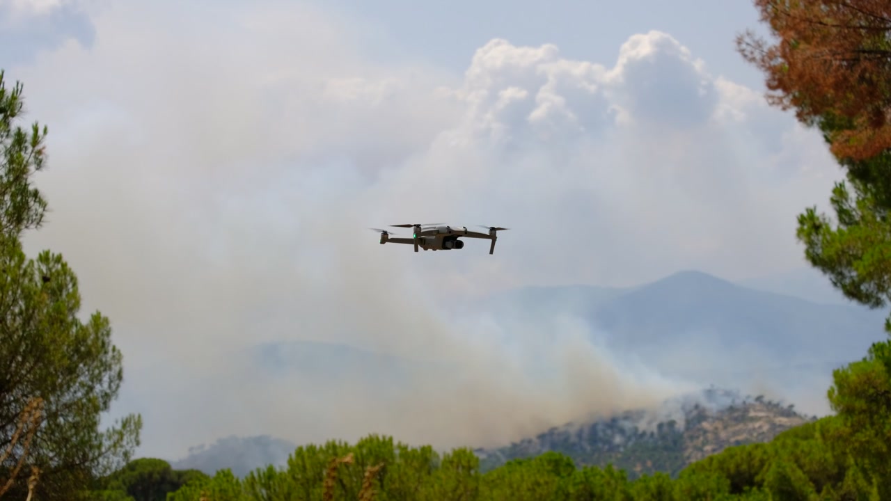 Drone vola sopra un incendio boschivo montano fumoso durante un'operazione di sorveglianza aerea vicino alla Valle de Iruelas e al bacino di El Burguillo