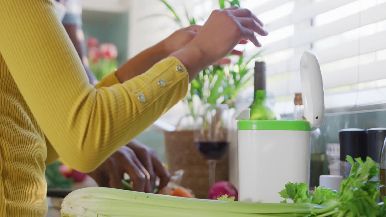 video de la sección media de una pareja diversa preparando comida juntos en la cocina, compostando verduras
