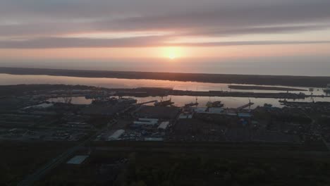 the sun is setting on a calm autumn evening as aearila looks out over an industrial city district with port infrastructure and production buildings