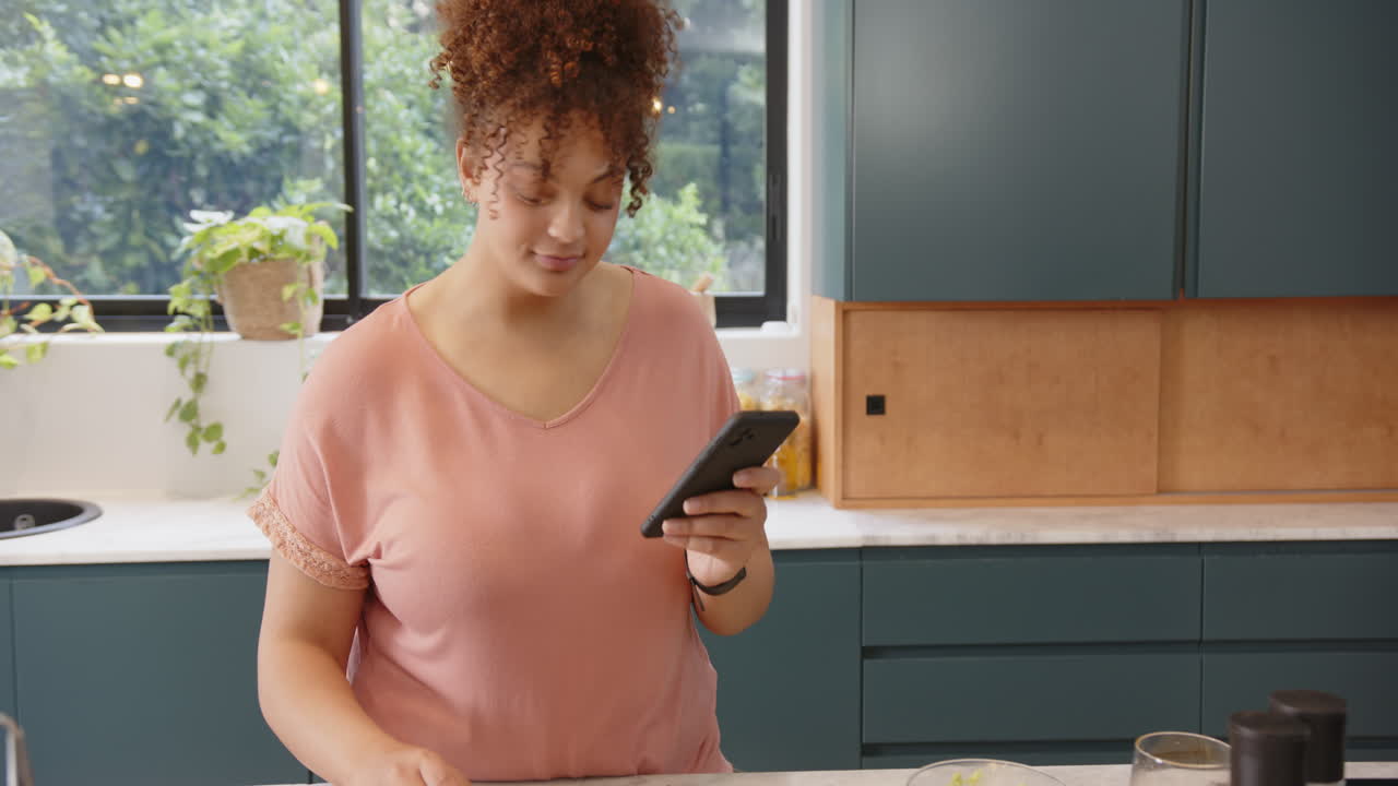 Eating snack and using smartphone, woman enjoying break in kitchen