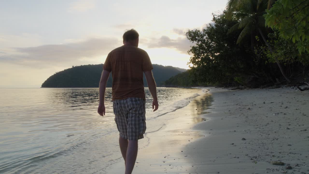 un hombre se pasea por la playa de arena de la isla de kri en raja ampat, indonesia, al atardecer
