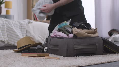 hombre luchando para empacar una maleta llena en el dormitorio en casa para las vacaciones de verano